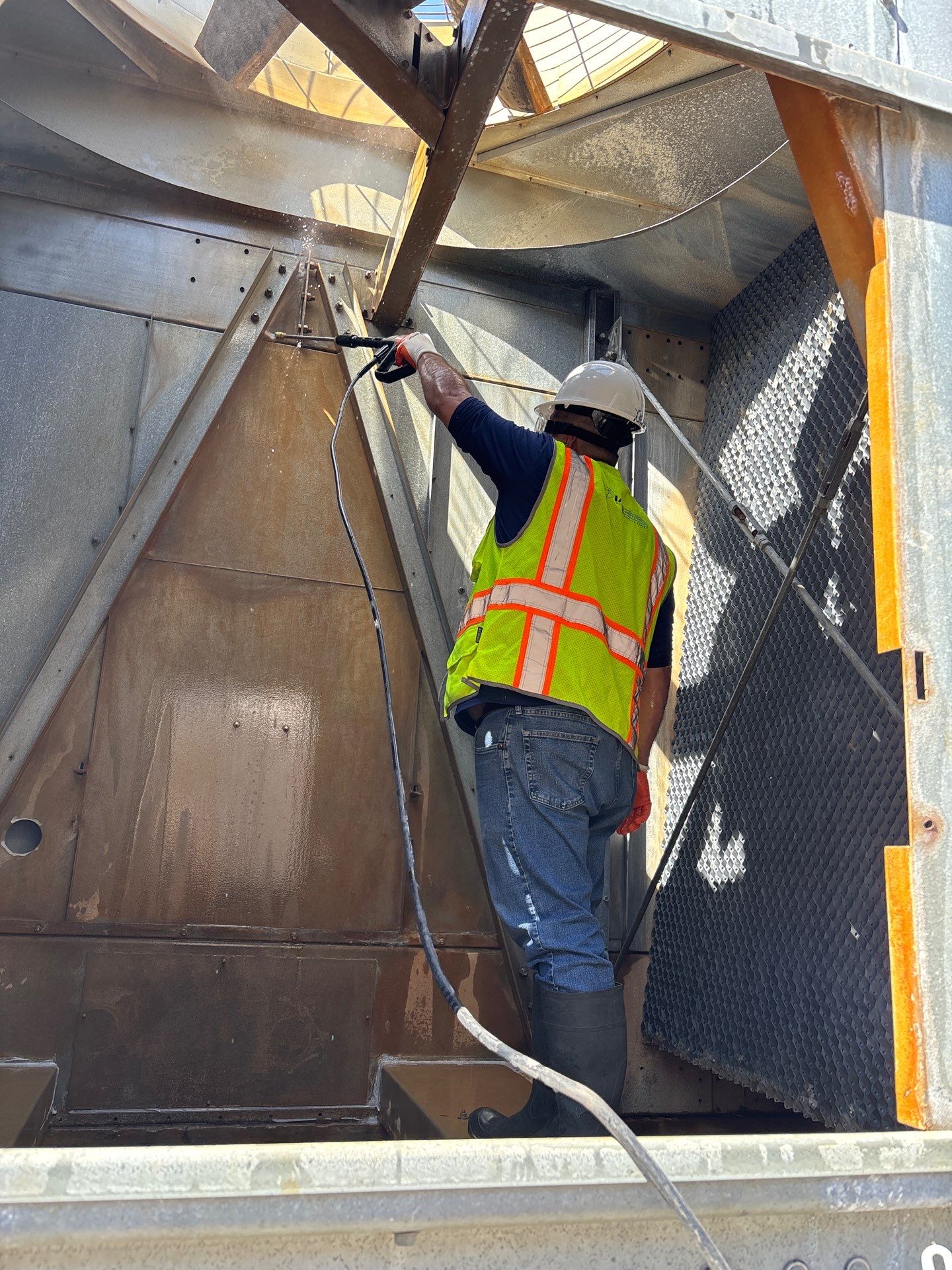 IAQ Restoration technician pressure-washing the plenum and fill inside a commercial cooling tower