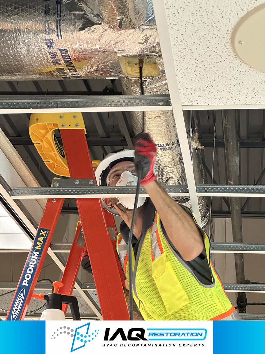 Technician applying HVAC duct decontamination treatment overhead